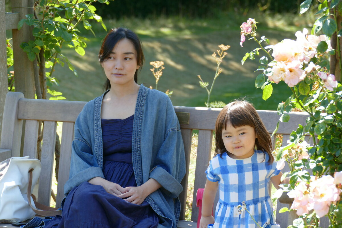 A mum and daughter sitting on a bench with roses